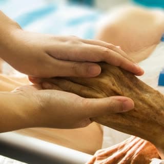 A nurse holding an elderly patient’s hand